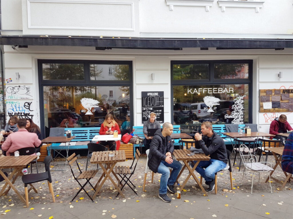 Front view of the coffee bar Aprilkind in Berlin with guests sitting in front of it.