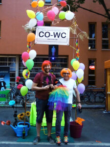 Two people in wigs at the information booth with the CO-WC sign and mascot.