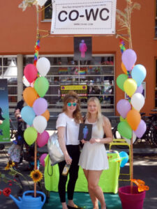 Visitors to the Lesbian and Gay City Festival stand in the CO-WC information booth holding the sign.