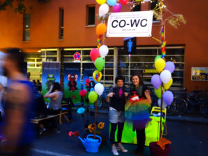 CO-WC info booth at night with two visitors of the Lesbian and Gay City Festival.