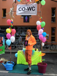 Visitors to the Lesbian and Gay City Festival at the CO-WC information booth, dressed in orange and holding the umbrella sign.