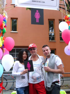 Shinhee Chae with the CO-WC sign and two visitors to the Lesbian and Gay City Festival.