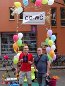 Two people at the Lesbian and Gay City Festival holding the CO-WC sign.