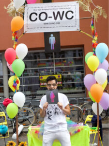 Visitor of the Lesbian and Gay City Festival stands in the CO-WC info booth and bites on the sign.
