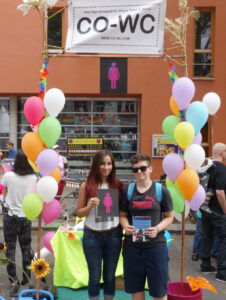 Two young people stand in the information booth with a CO-WC sign and flyer.