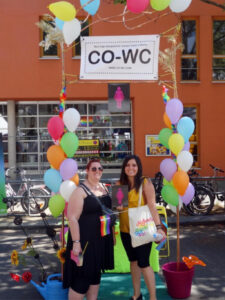 Two people in front of the CO WC info booth, with the sign and a rainbow flag.
