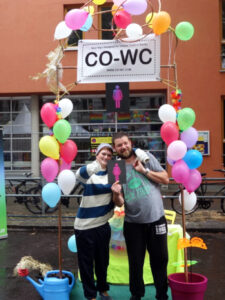 Two people are standing in front of the CO-WC info booth and one person is giving the thumbs up.