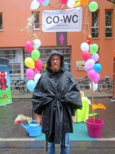 Paul Jonczyk stands in a raincoat in front of the CO-WC information booth.